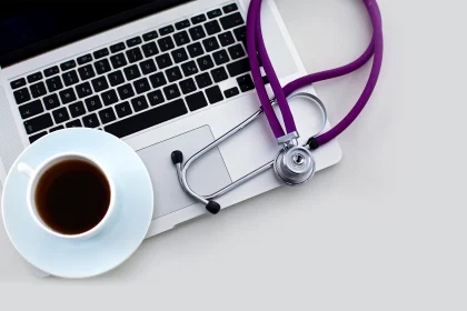 A medical stethoscope near a laptop on a wooden table on white