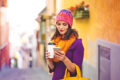 Woman in city holding coffee mug and looking at mobile phone