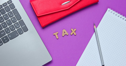 字母T-A-X排列在紫色的背景上，周围是办公桌配件