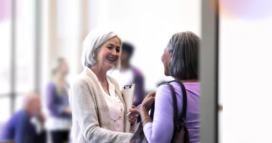 mature adult female group leader smiles in welcome as she shakes hands with a new member.