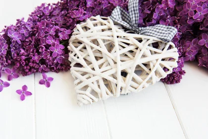 Purple lilac flowers on a table with a heart and bow.