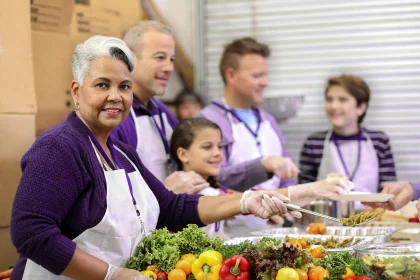 woman smiling while serving food with a group of volunteers at soup kitchen