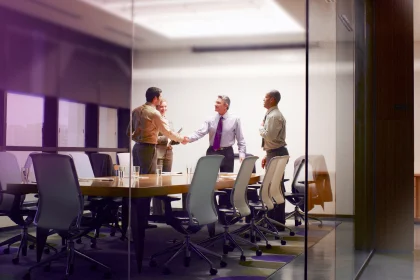 Four businesspeople in boardroom with two shaking hands