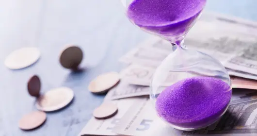 Image of hourglass sitting on top of money