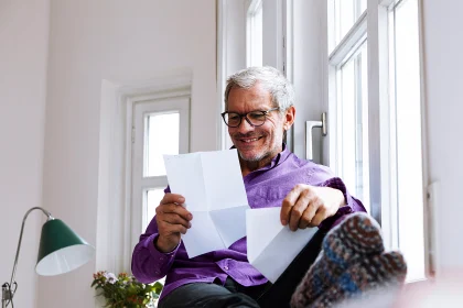 Mature man at home sitting at the window smiling while reading documents 