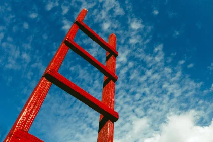 Red wooden ladder leading up to a blue sky