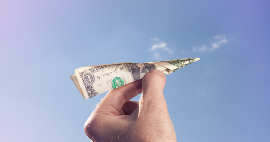 Hand holding paper airplane made of money