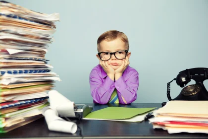 Stressed kid sitting between pile of documents and old fashioned telephone