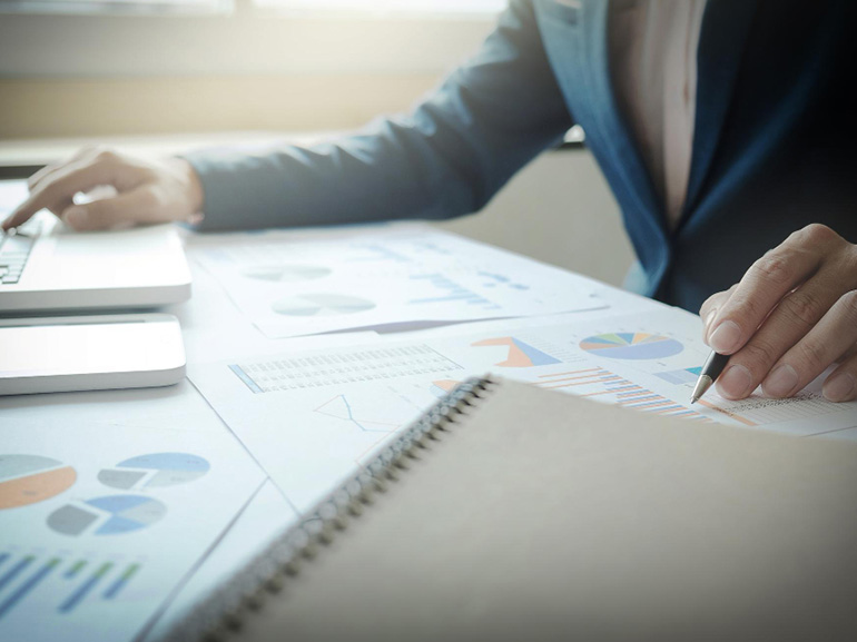 Geschäftsmann, der an einem Schreibtisch an einem Laptop arbeitet und dabei Diagramme und Grafiken analysiert