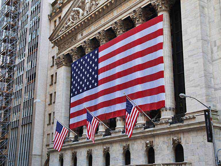Wall Street building with a big US flag on the front and waving smaller flags
