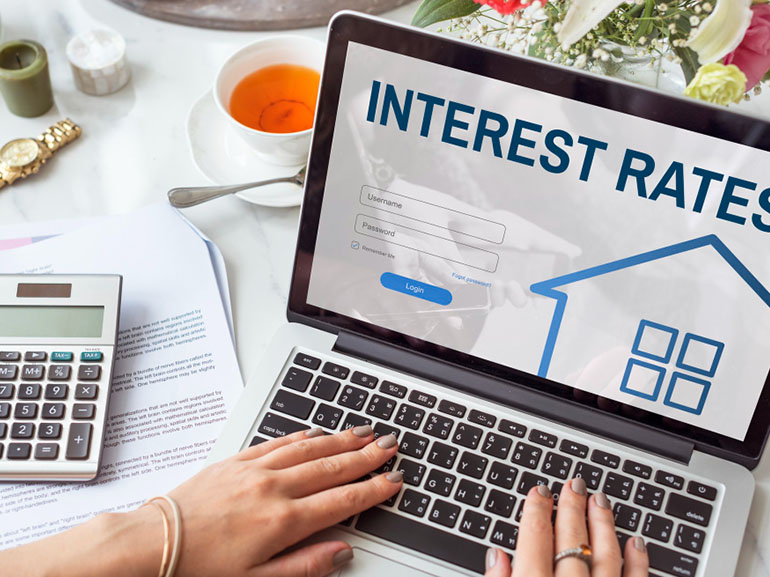 Laptop-Bildschirm zeigt Zinssätze mit Taschenrechner und Dokumenten.