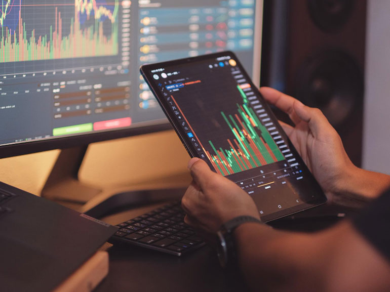 Person analyzing stock market charts on a tablet and computer monitor