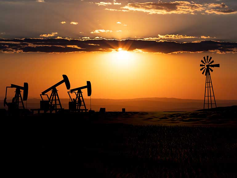 Oil pumps and wind mill during sunset