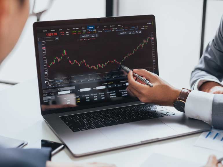 A business meeting analysing a broker screen with graphs on a laptop