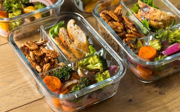 Two glass containers filled with meal prep of chicken, mixed nuts, and assorted vegetables.