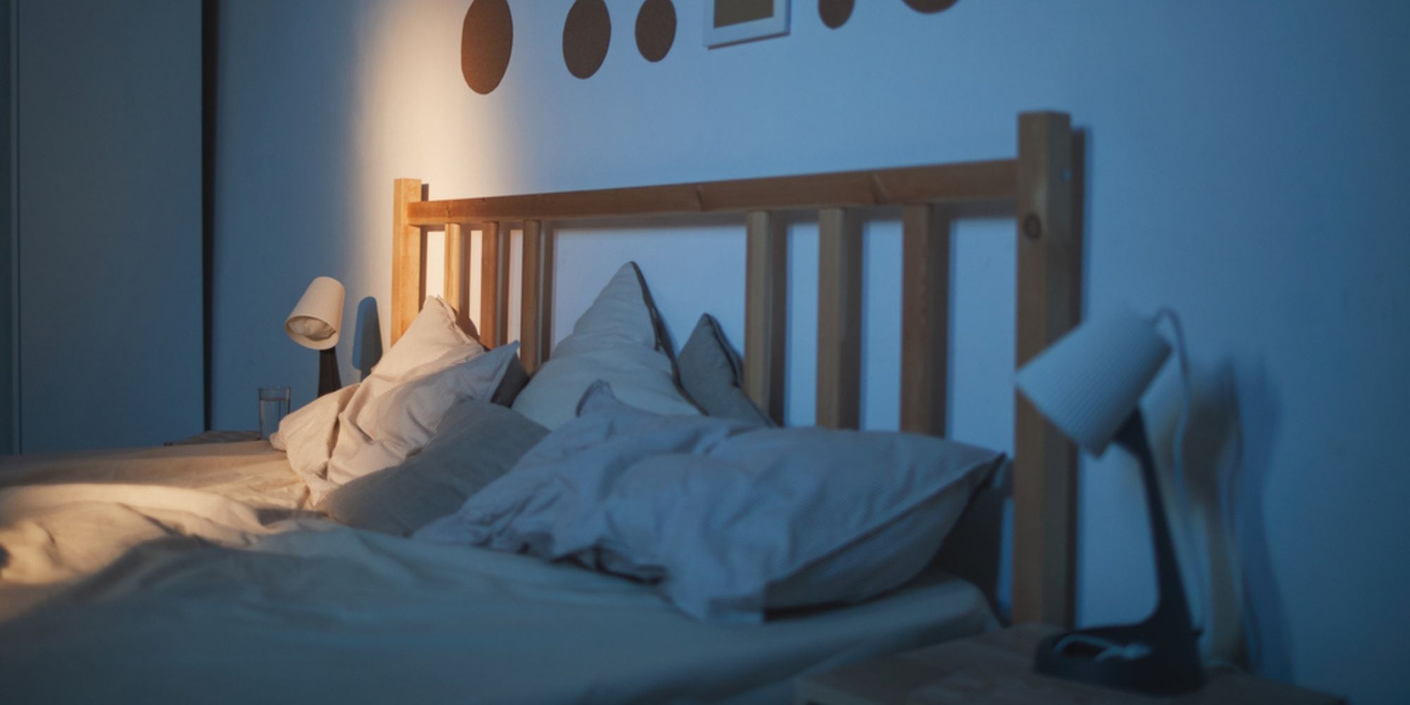 Empty bed at night with tousled pillows and light shining from the bathroom.