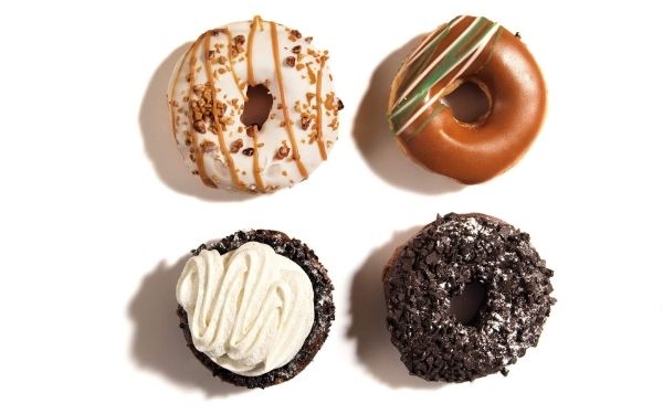 Four doughnuts laying next to each other against a white background all with different toppings.