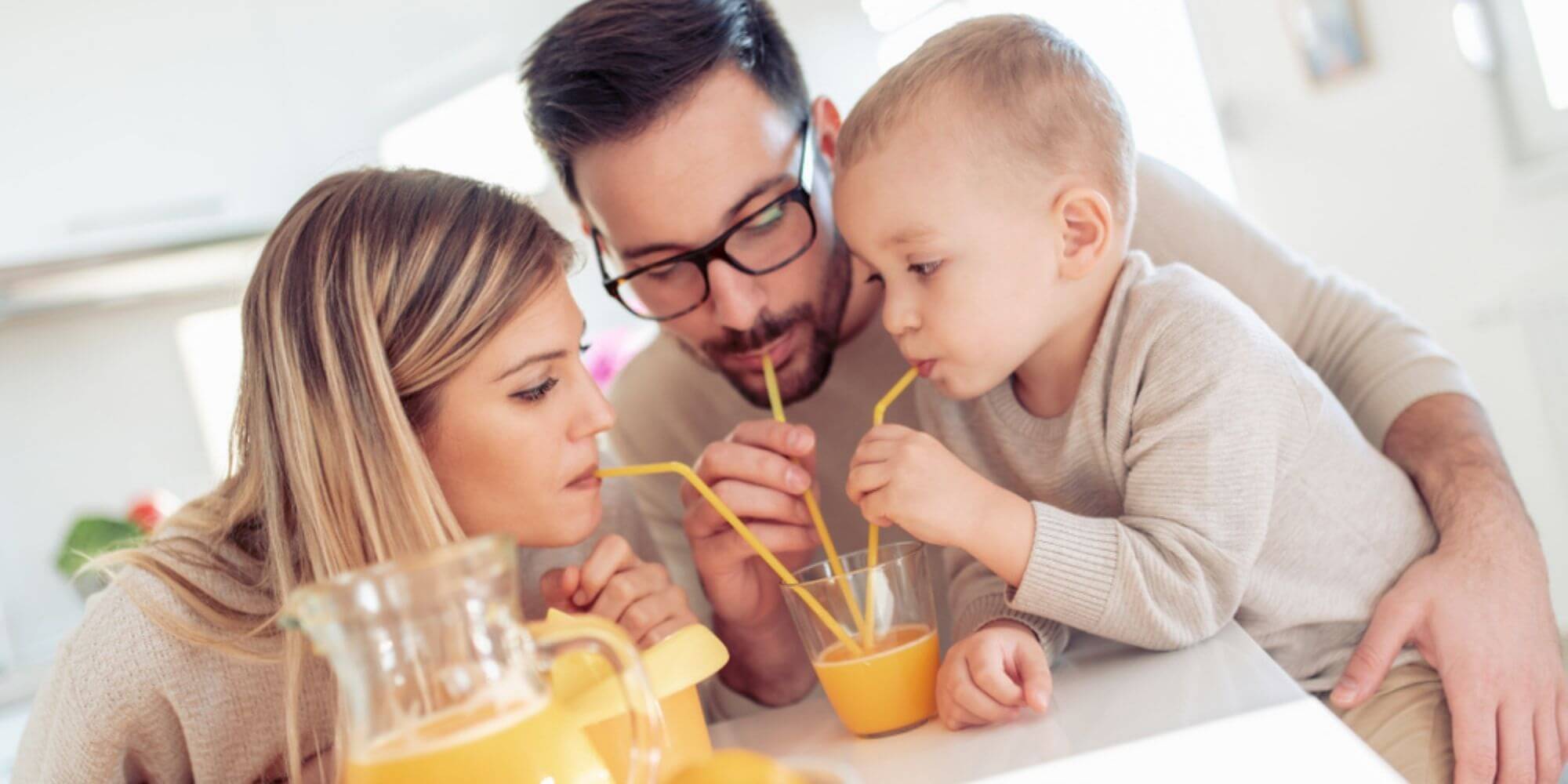 A mother, father, and son drinking homemade orange juice from straws in the same cup.
