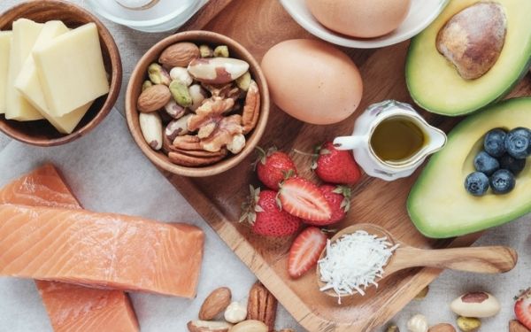 Aerial view of salmon, nuts, cheese, strawberries, eggs, avocados and coconuts on a wooden board.