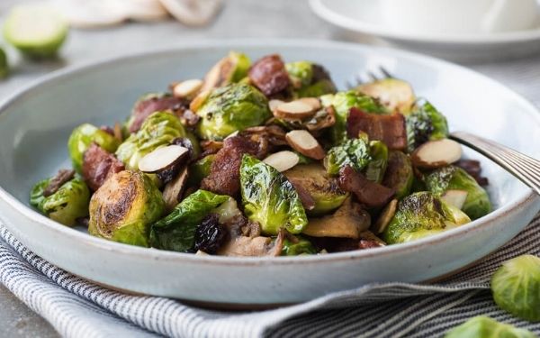 Bacon and brussels sprout hash in a gray bowl with a fork sitting on top of a napkin.