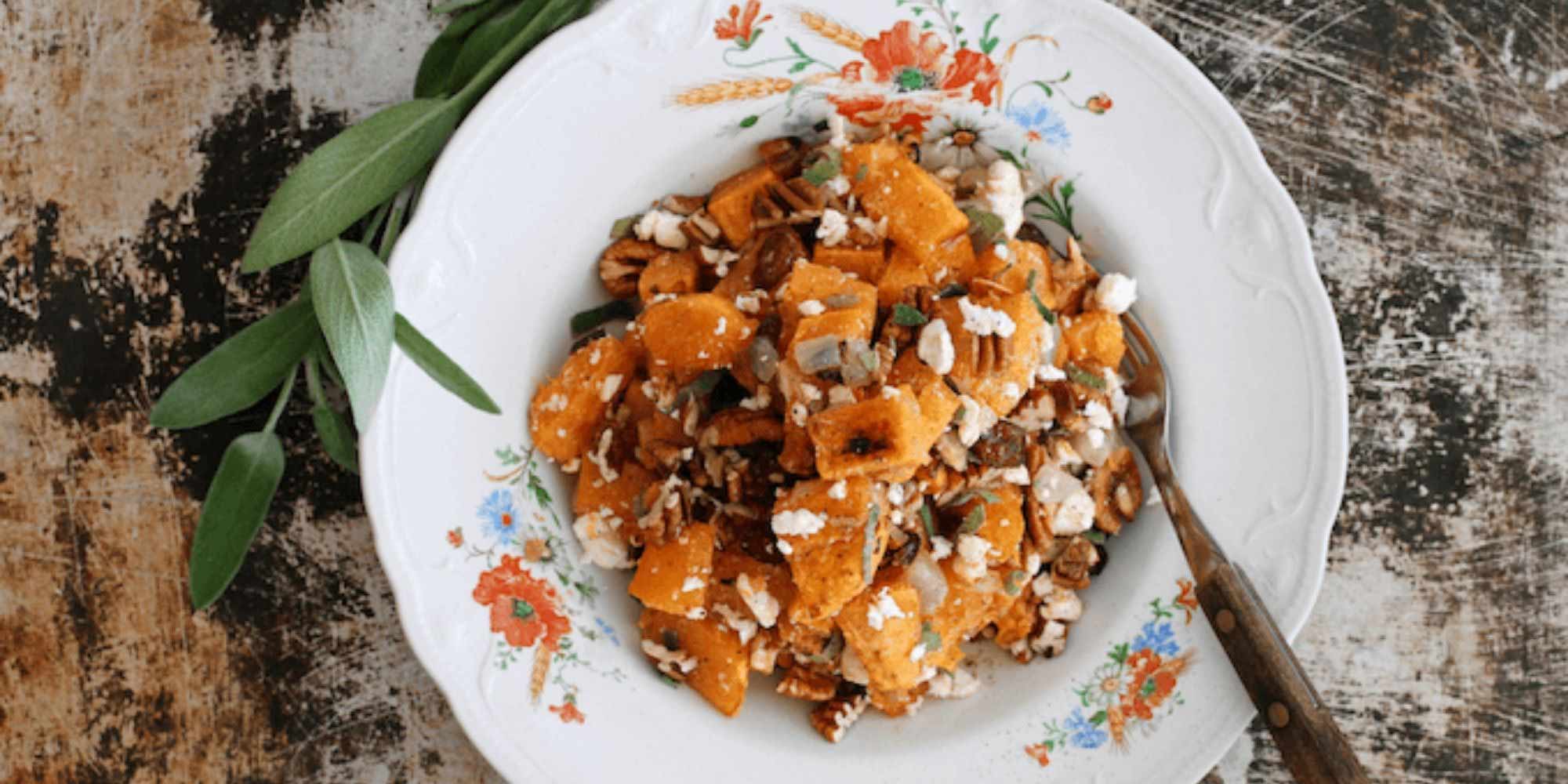 Butternut squash salad with feta cheese in a white bowl on a wooden table with a fork.