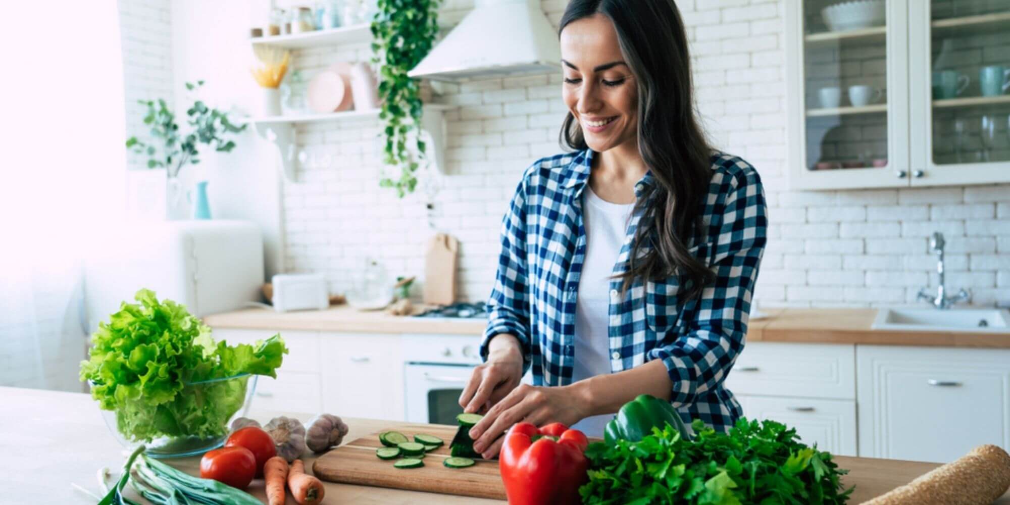 Young woman chopping vegetables on wooden cutting board in sunlit kitchen.