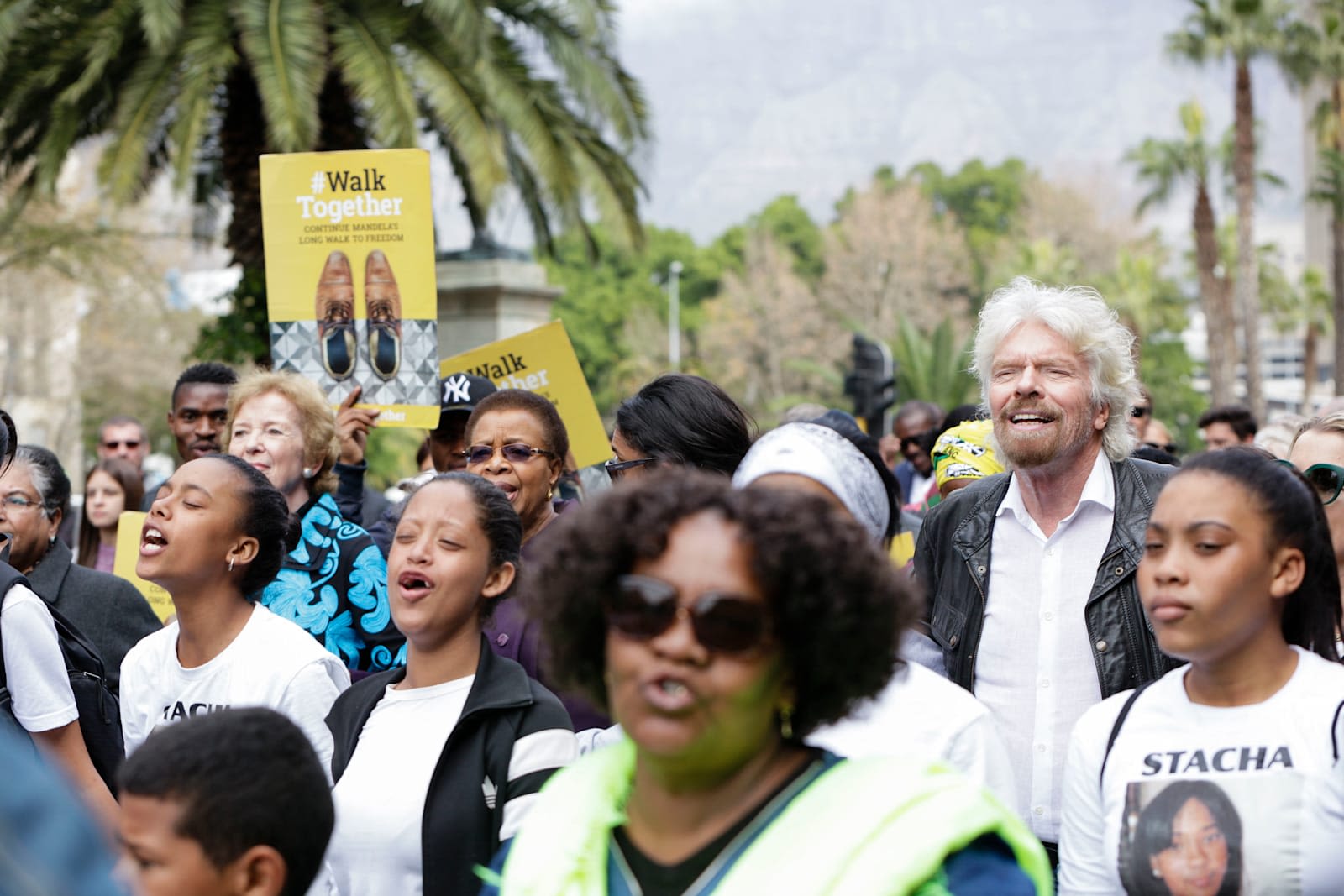 Richard Branson walking with elders some of whom are holding up signs 