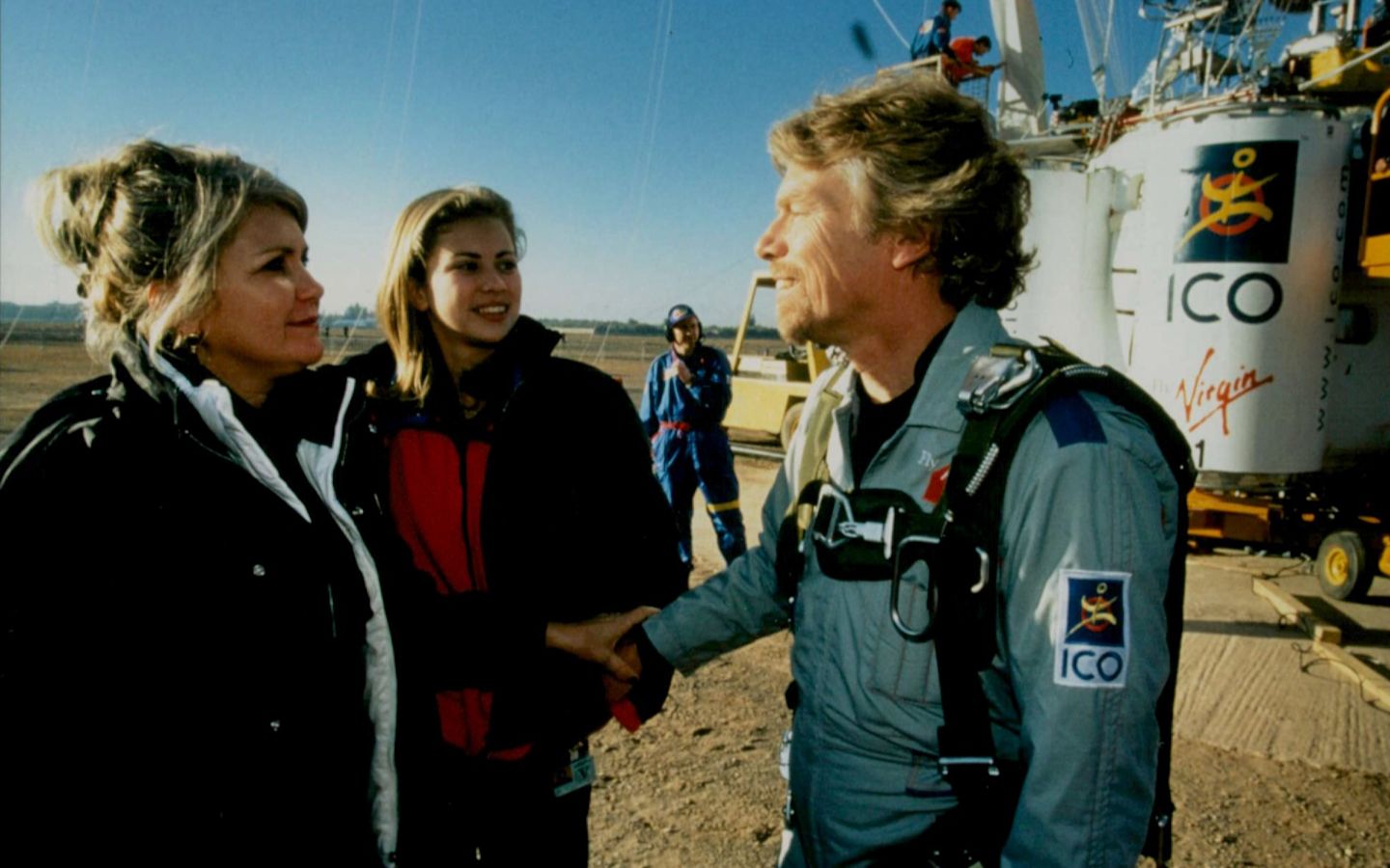 Richard Branson speaking to Joan Branson and Holly Branson in front of a hot air balloon