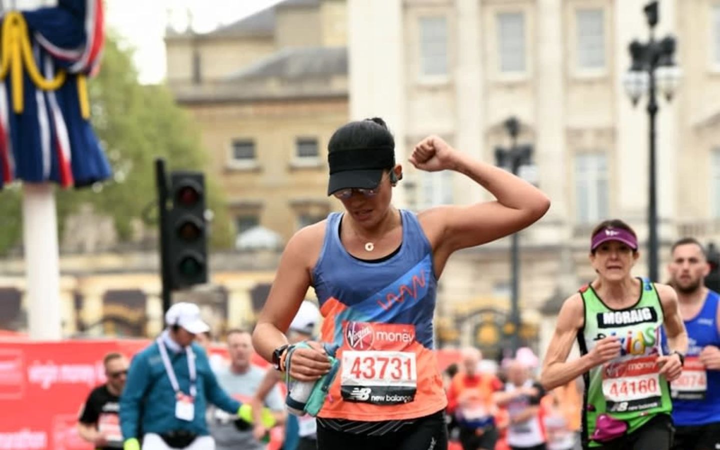 Runner, Lisa Kurdziel wearing black baseball cap raising fist in the air with runners behind her