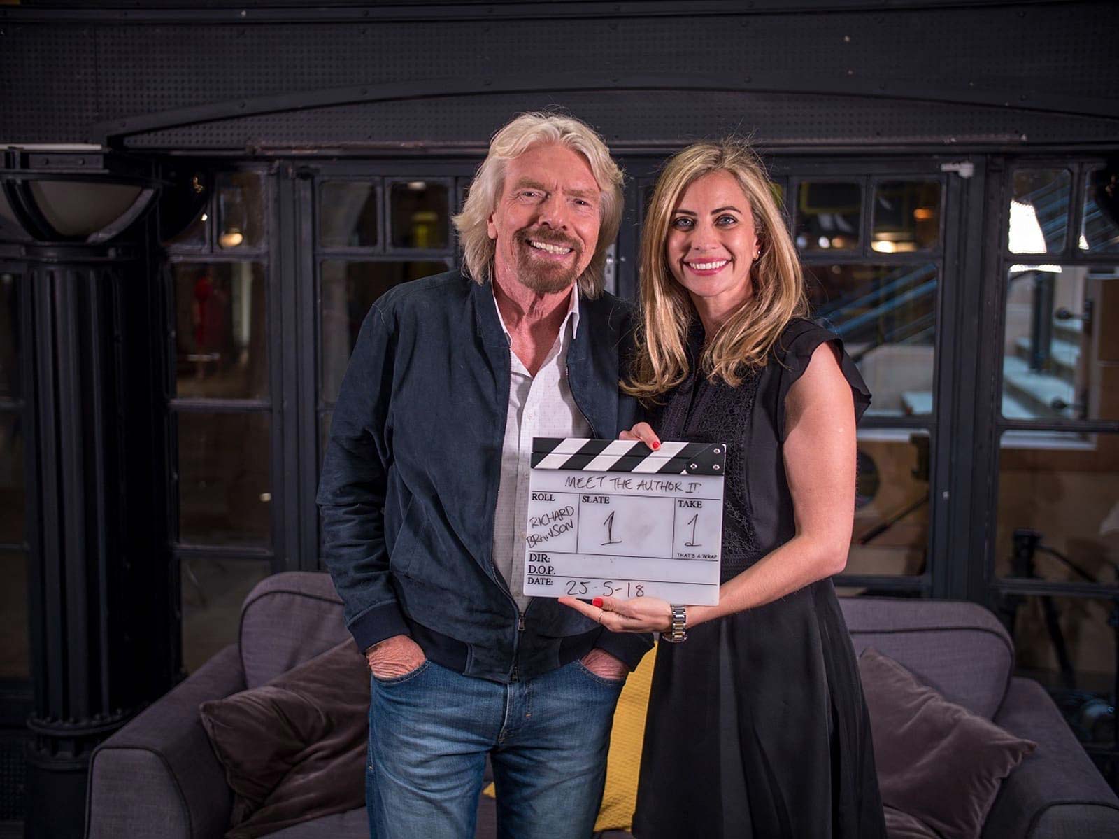Richard and Holly Branson standing smiling at the camera, Holly is holding a clapperboard