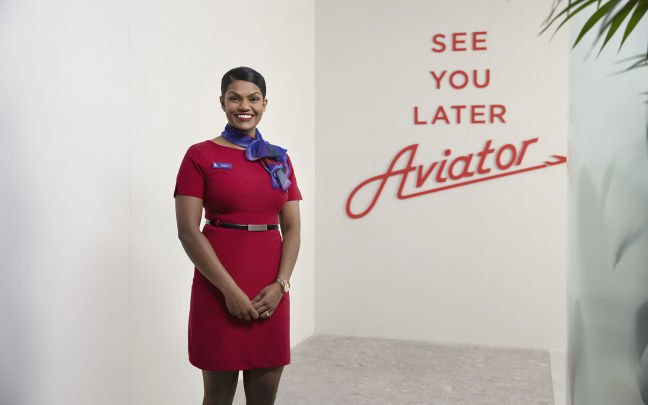 A member of Virgin Australia cabin crew poses in front of a sign that reads "See you later aviator"
