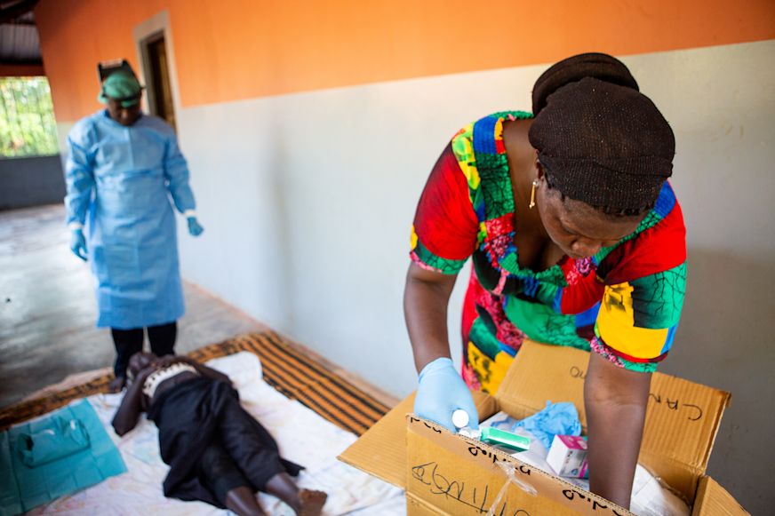 Dionesa, nurse assistant, grabs surgical materials while Forma preps Nene for trachoma surgery on the porch of her home | Sightsavers/Alyssa Mariner