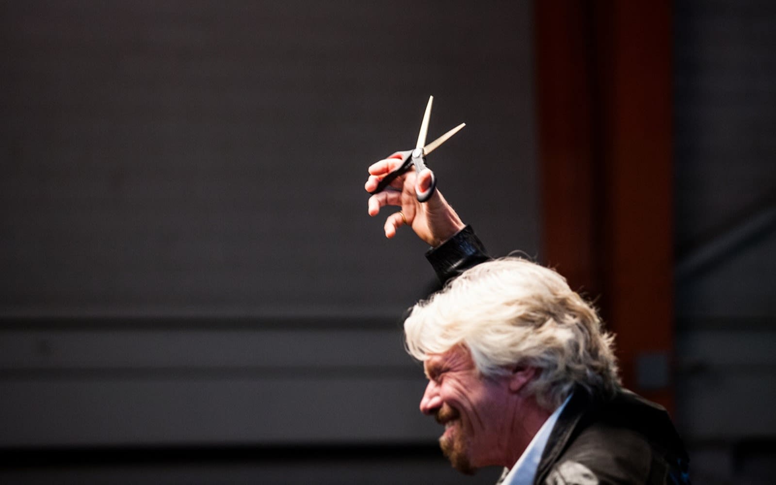 Richard Branson smiling and holding scissors in the air