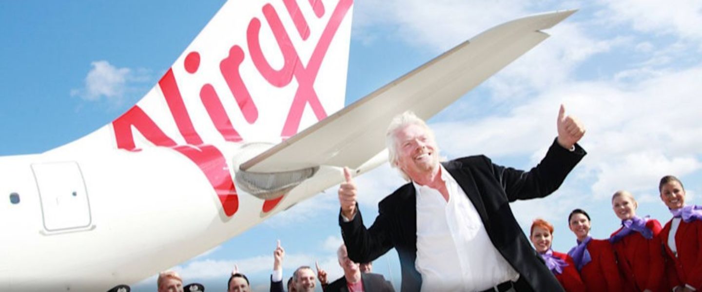 Richard Branson stands smiling with thumbs up, with a Virgin Aircraft and its crew