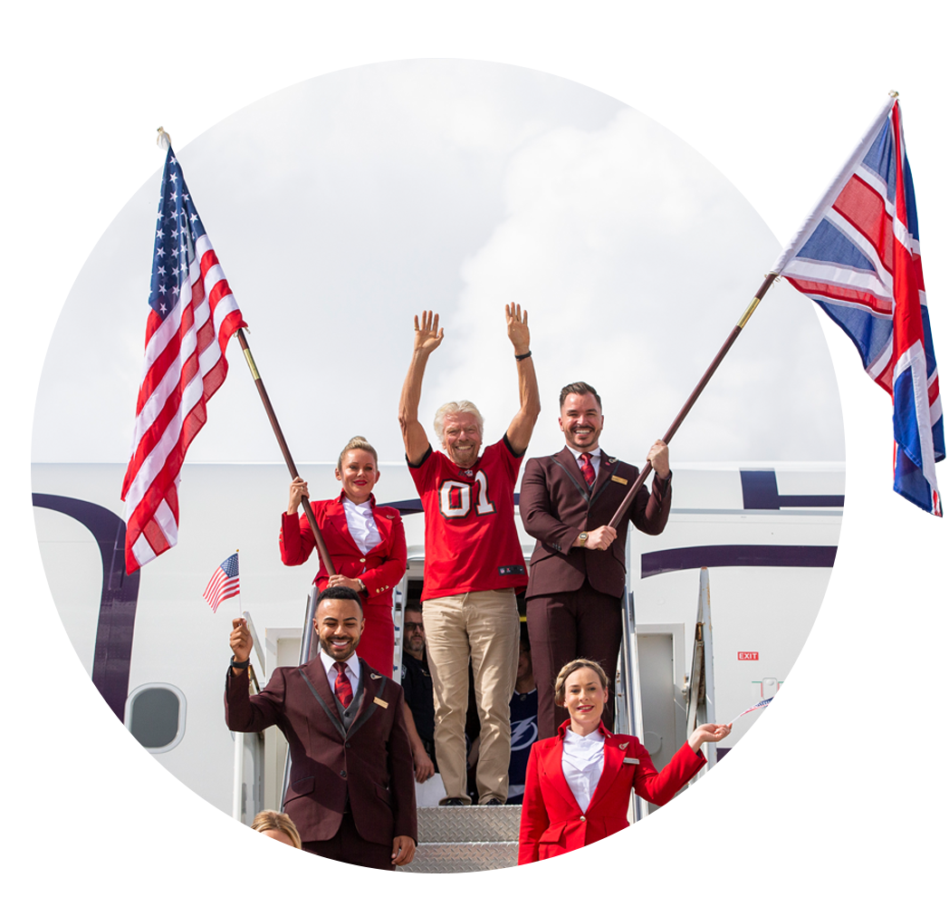 Richard Branson climbing down the steps from an Airbus A330neo aircraft in Tampa, Florida, with two Virgin Atlantic cabin crew holding UK and US flags