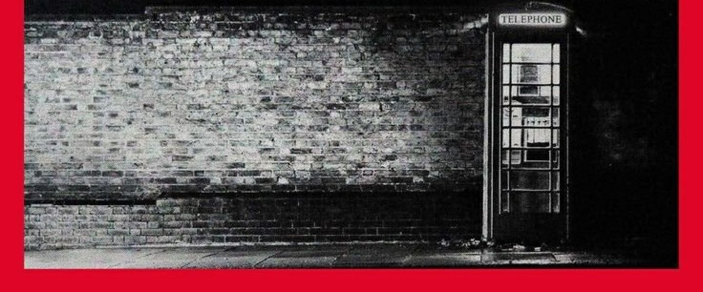 Black and white image of a telephone box against a brick wall. The image has a red border around it