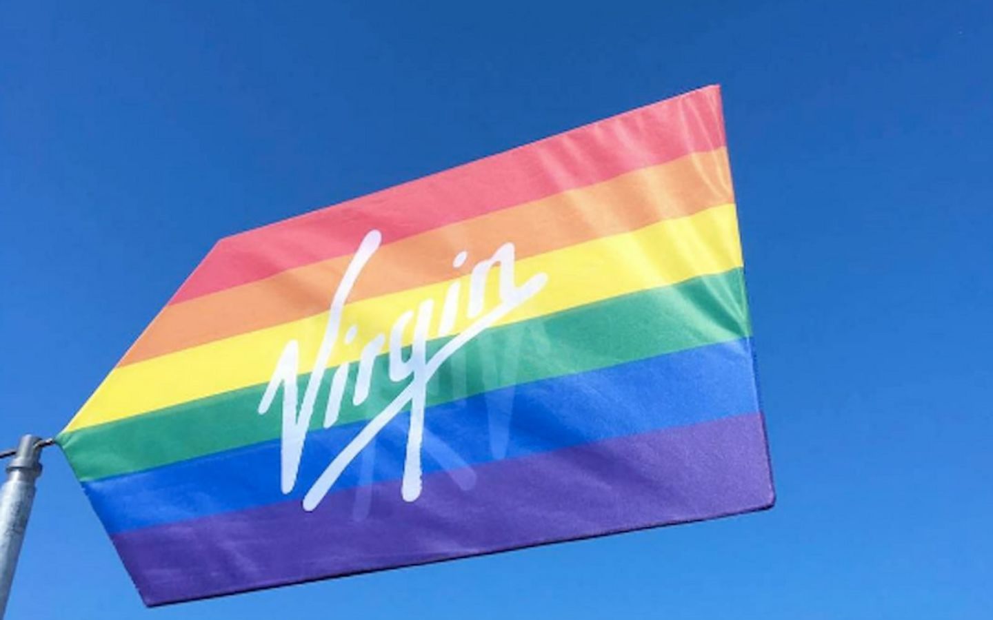 The Pride flag with the Virgin logo across it in white text