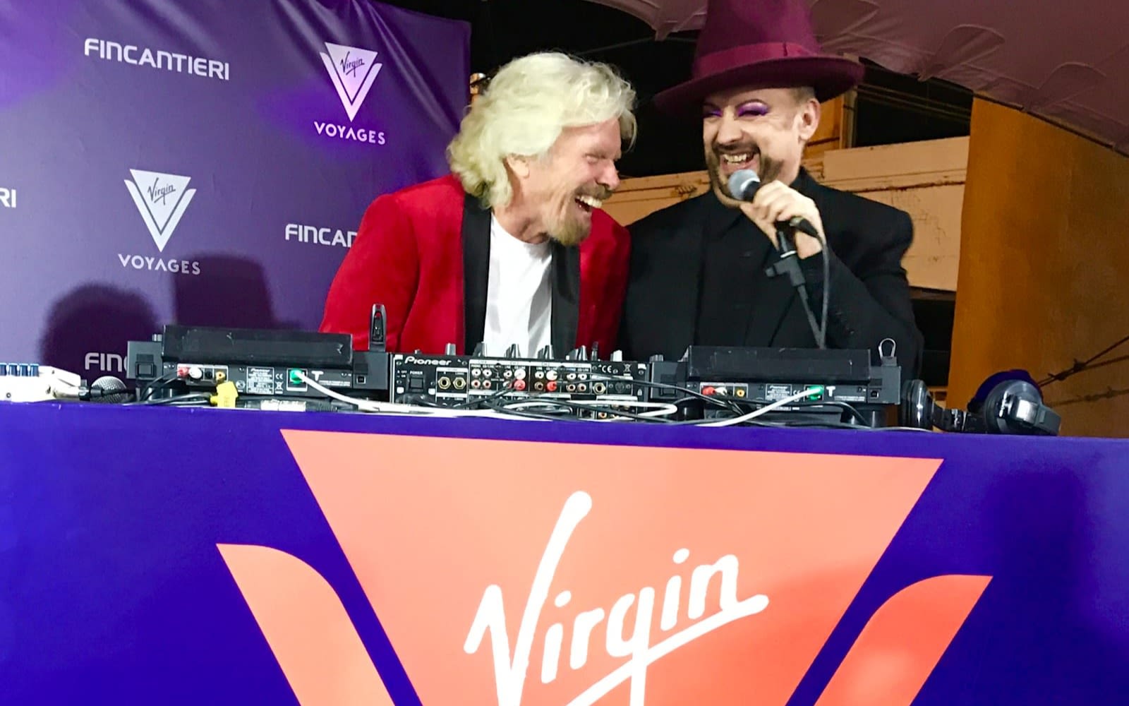 Rihard Branson stands behind decks with Boy George at the Virgin Voyages keel laying party
