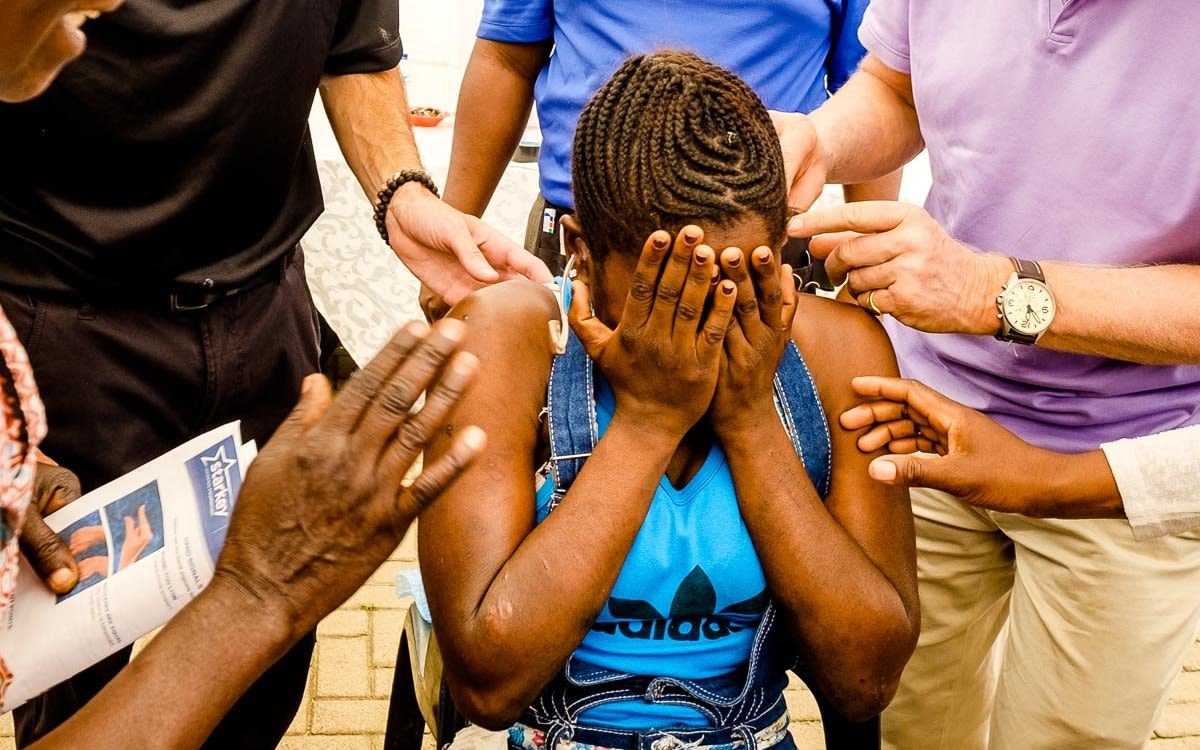 A young woman of colour, sits with her head in her hands, overcome with emotion at being able to hear for the first time.