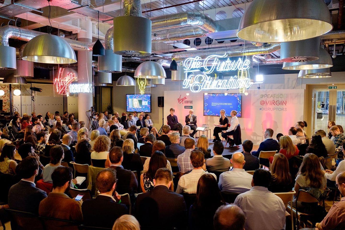 Four people on a stage, with an audience looking on