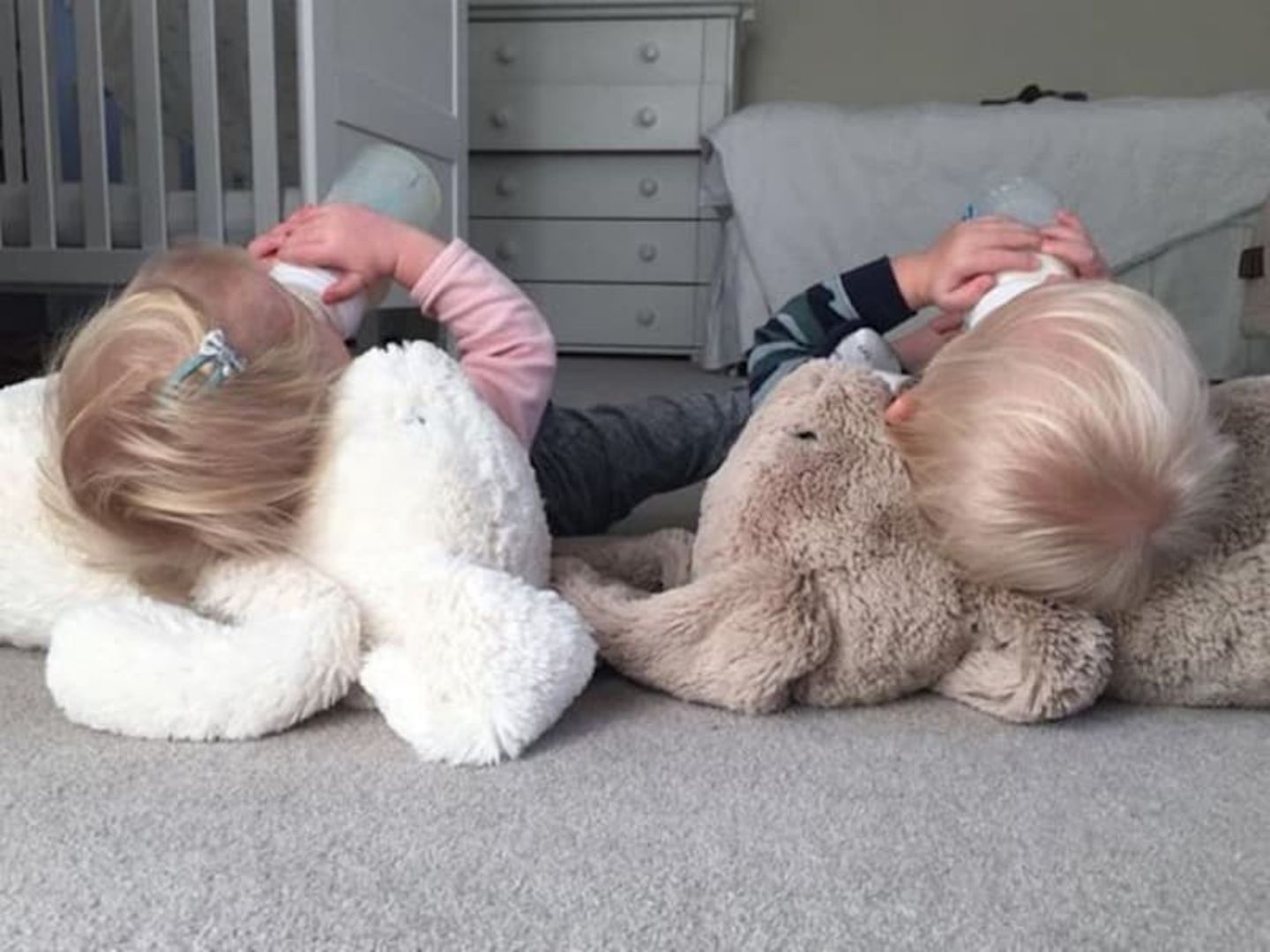 Etta and Artie lay on stuffed bunny toys, drinking a bottle