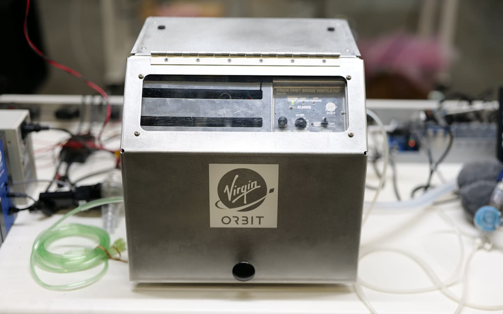 Silver cased ventilator on work bench with Virgin Orbit logo