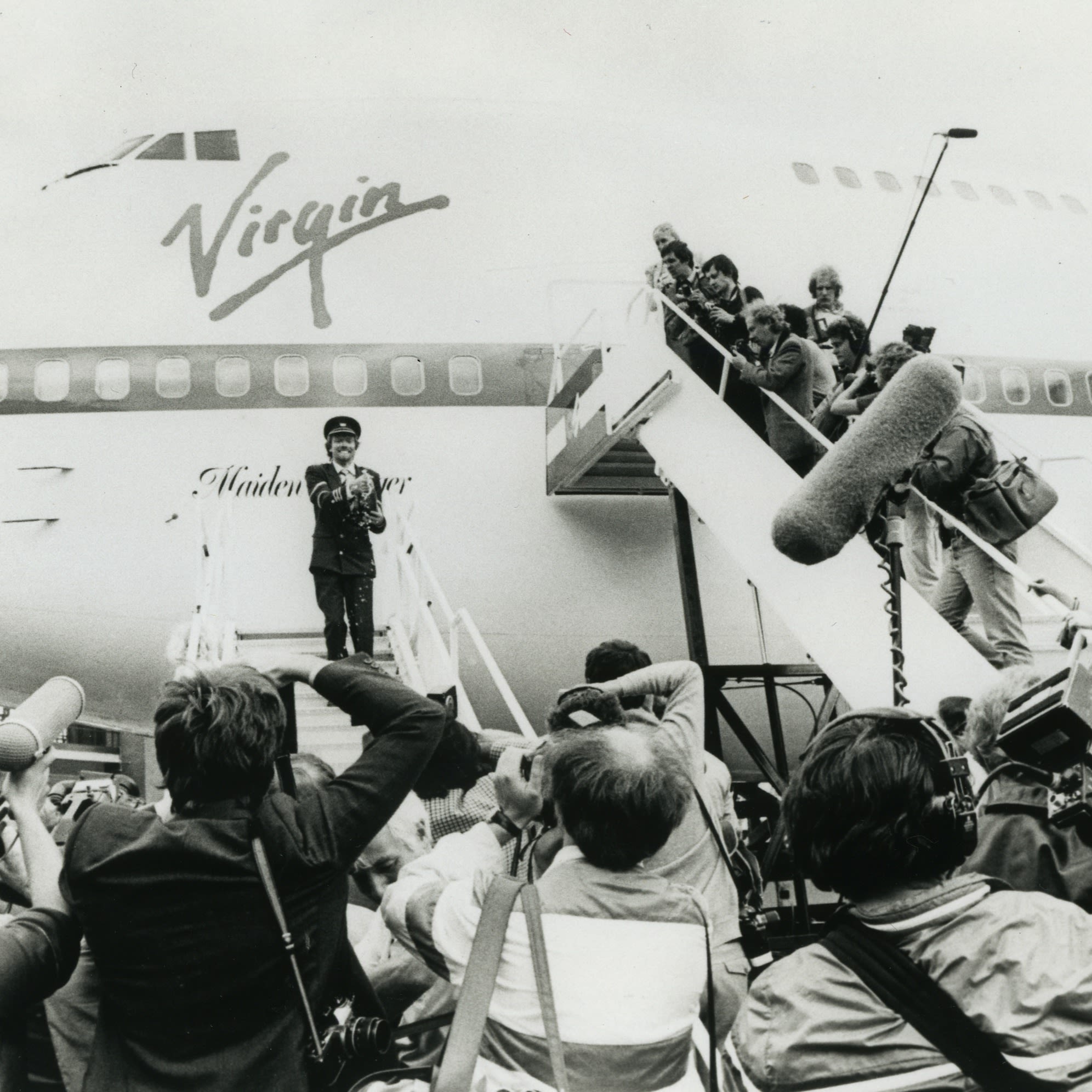 Richard Branson celebrating surrounded by the media in front of a Virgin Atlantic aeroplane