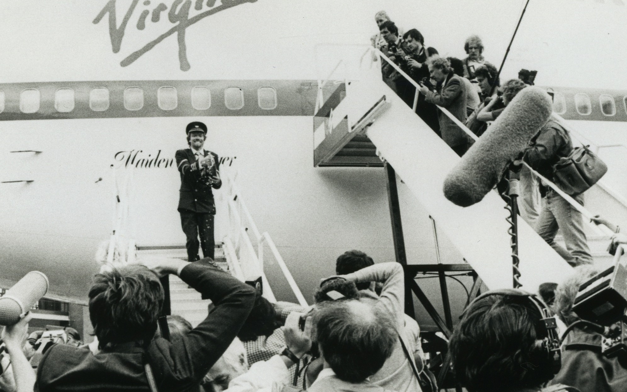 Richard Branson celebrating surrounded by the media in front of a Virgin Atlantic aeroplane