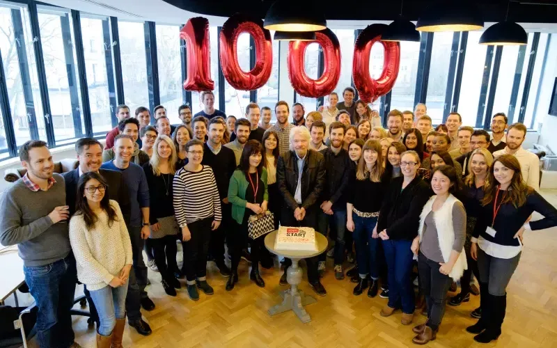 Richard Branson with Virgin Management employees in front of a cake to celebrate Virgin StartUp's 100th loan that they'd given out