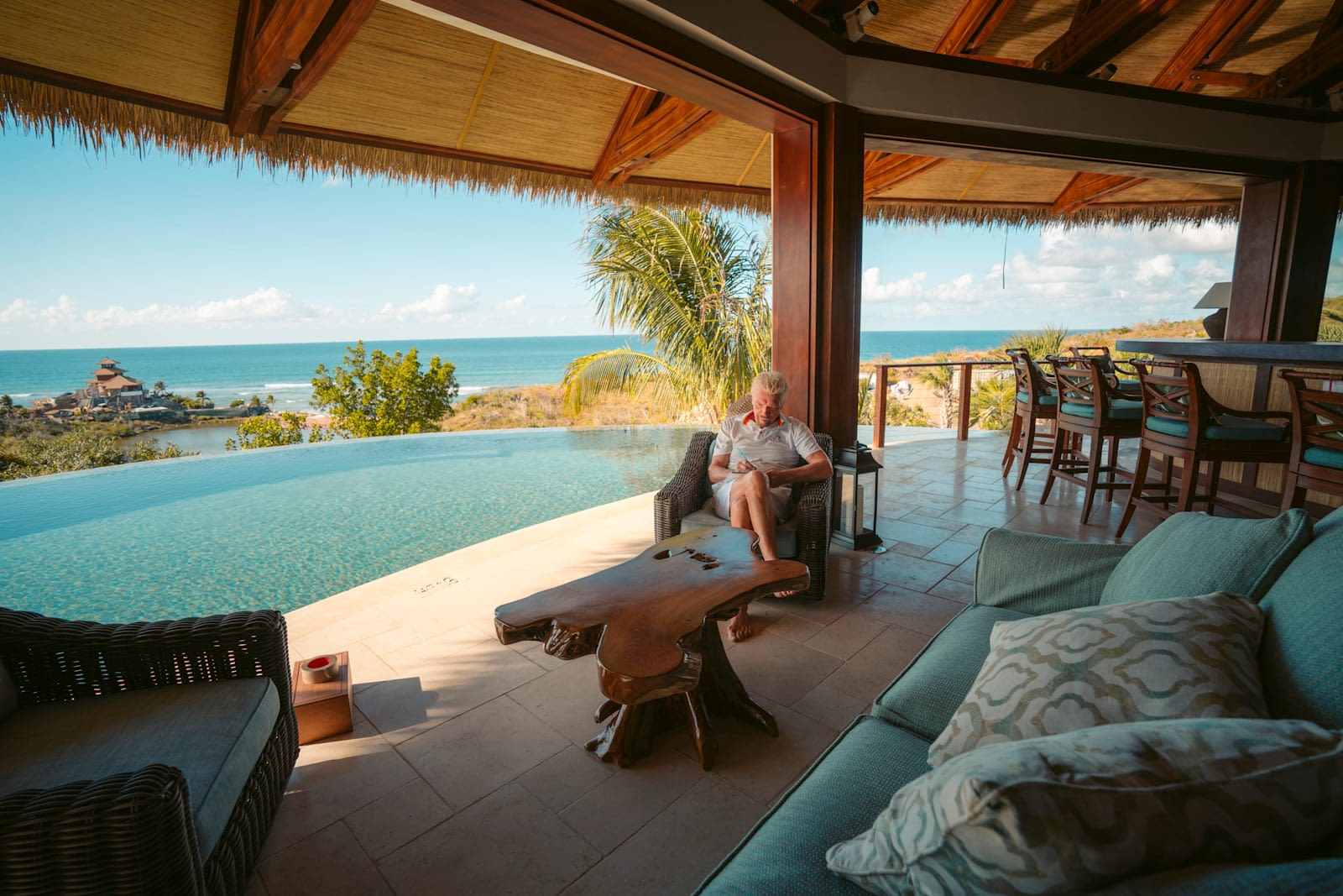 Richard Branson sitting by the pool on Necker Island, reading