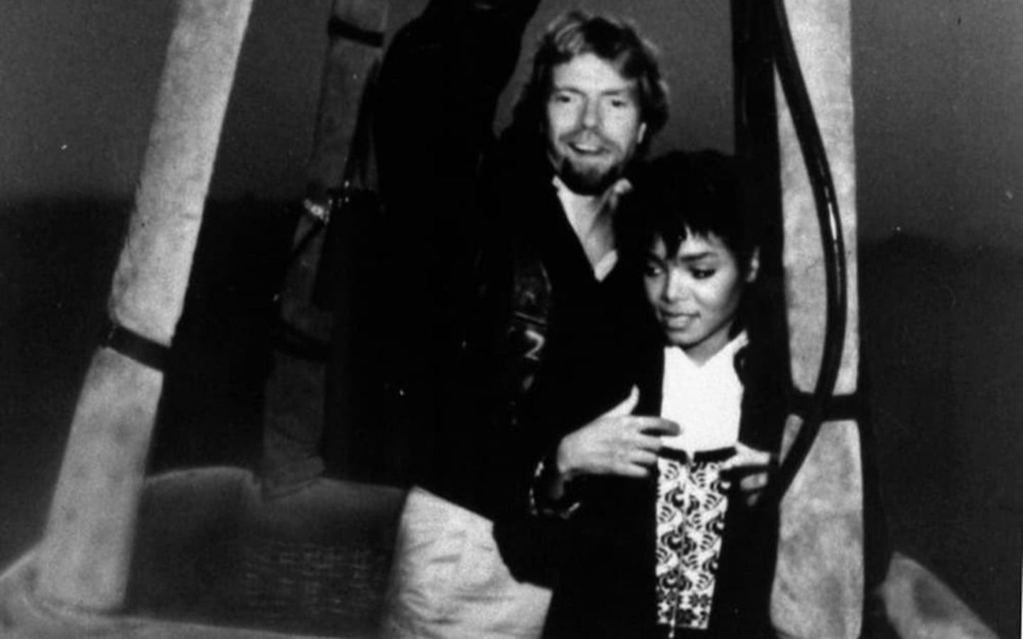 A black and white photo of a young Richard Branson with Janet Jackson, in the basket of a Virgin Balloon