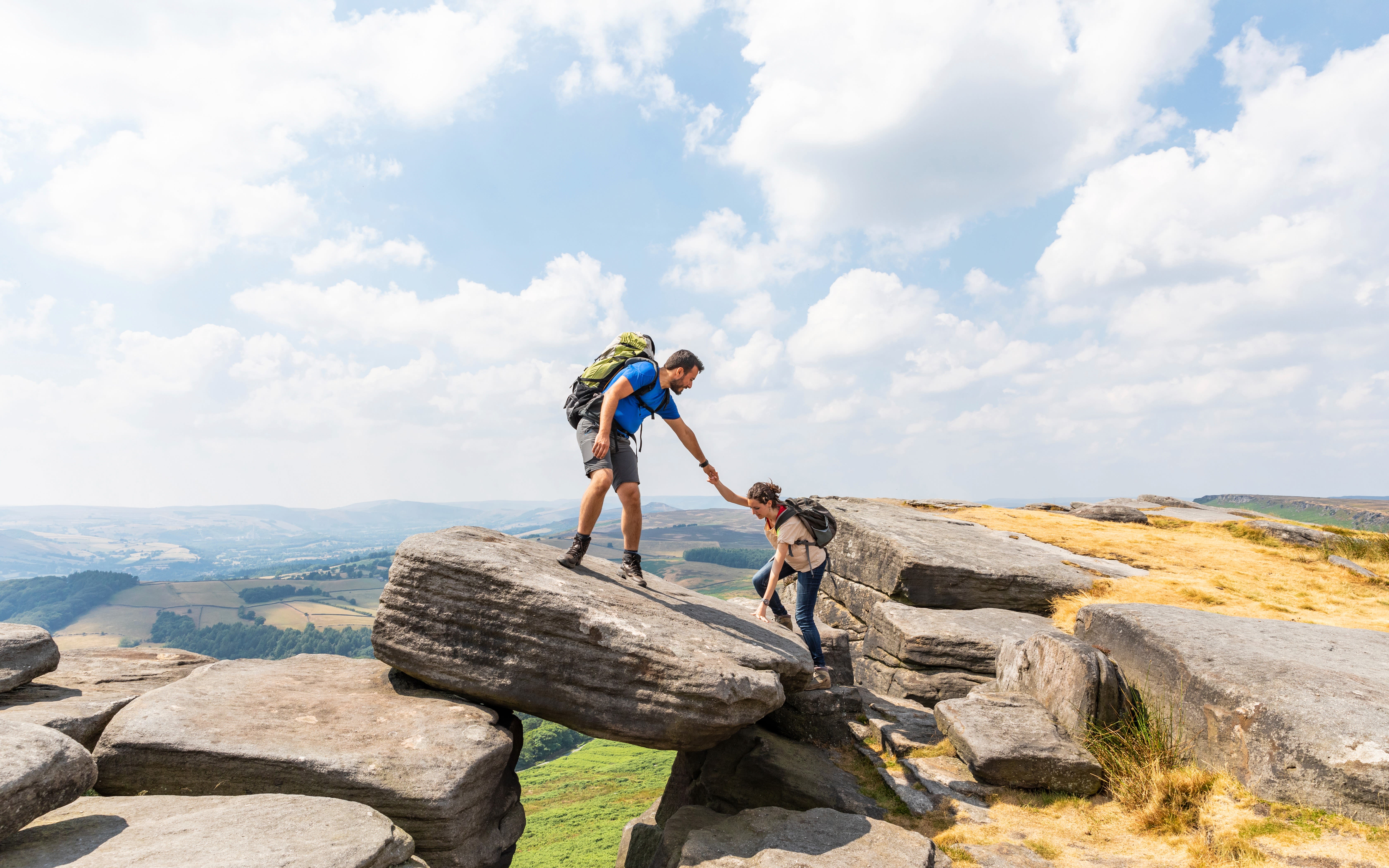 Image of a man helping a woman to climb to the top of a rock in the Peak District.