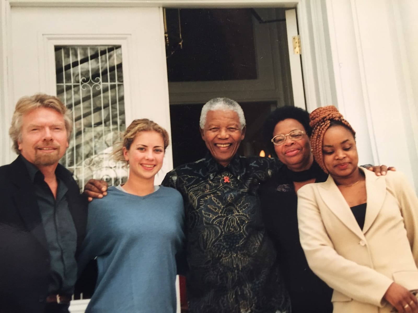 Richard and Holly Branson stand with Nelson Mandela.  They are smiling with their arms around each other's shoulders