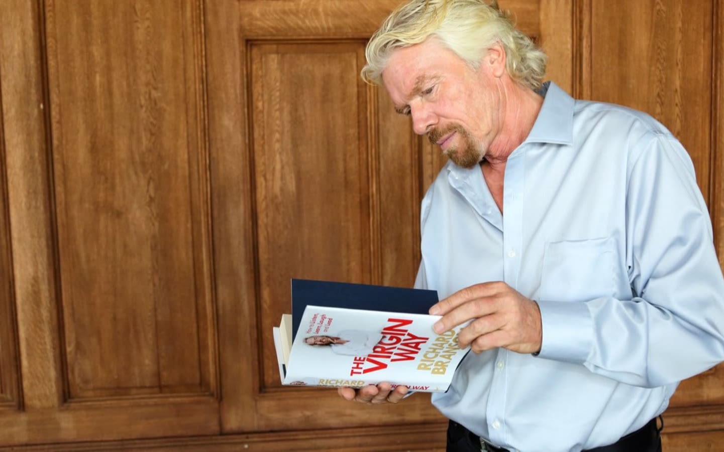 Richard Branson standing and reading his book The Virgin Way